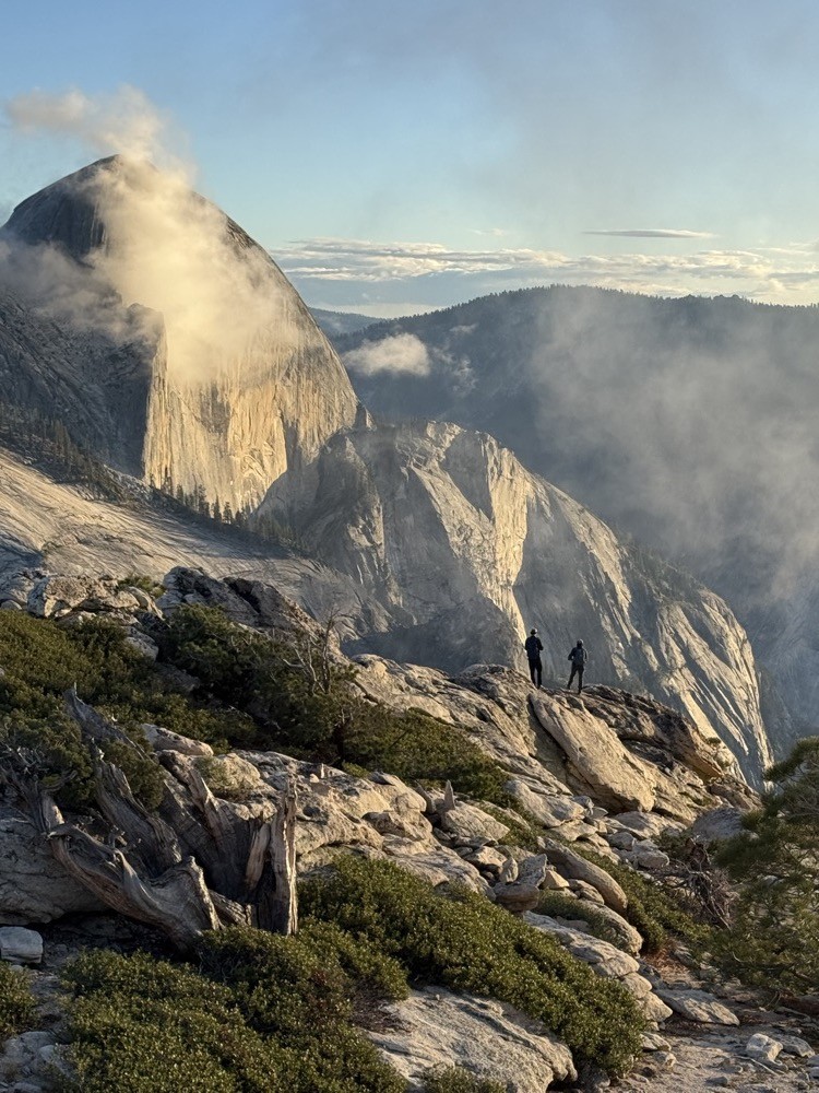 Two people on a granite ledge looking toward Half Dome in Yosemite